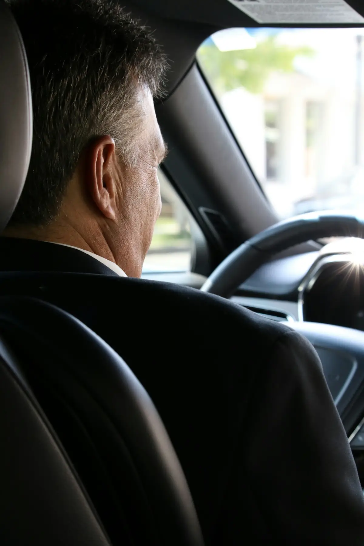 Motorista de terno escuro ao volante, visto do banco de trás