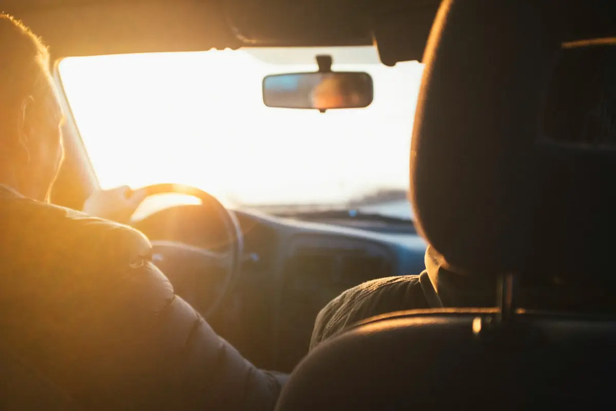 Driver at the wheel of a car, with golden late-afternoon light coming through the windshield