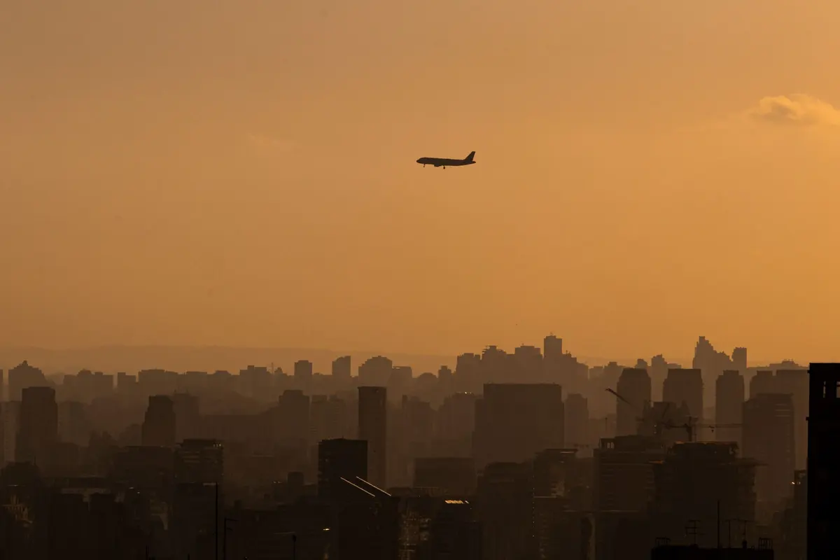 Airplane approaching São Paulo at sunset, over the silhouette of the buildings