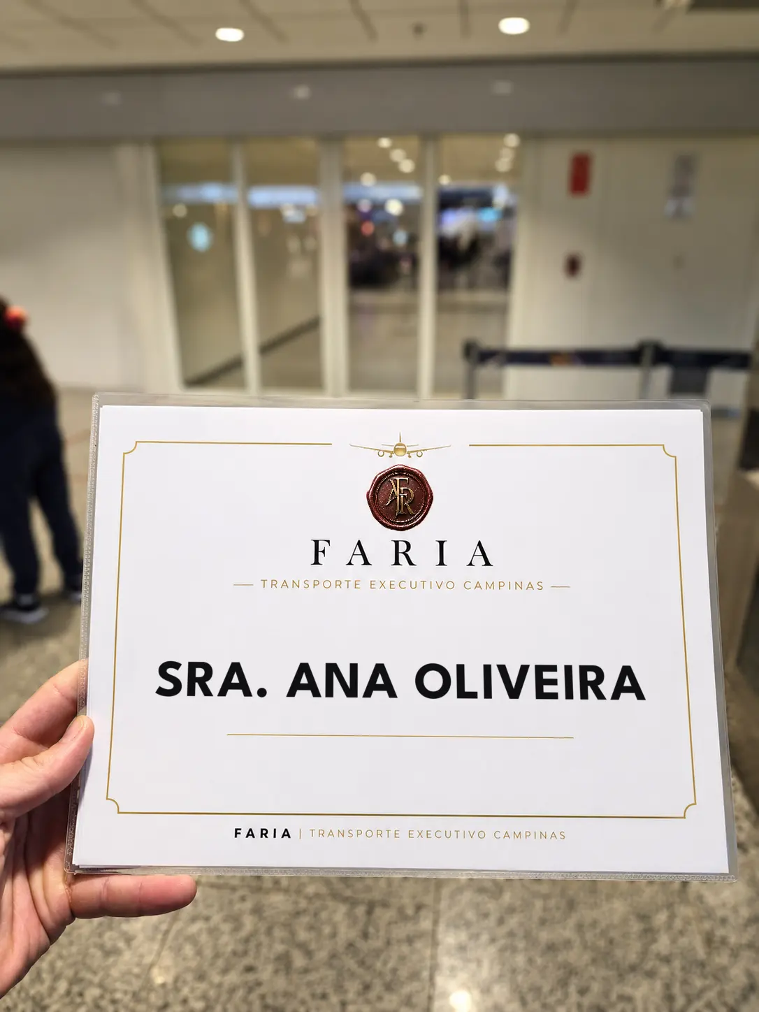 Name sign of Faria Executive Transport held up in an airport arrivals hall