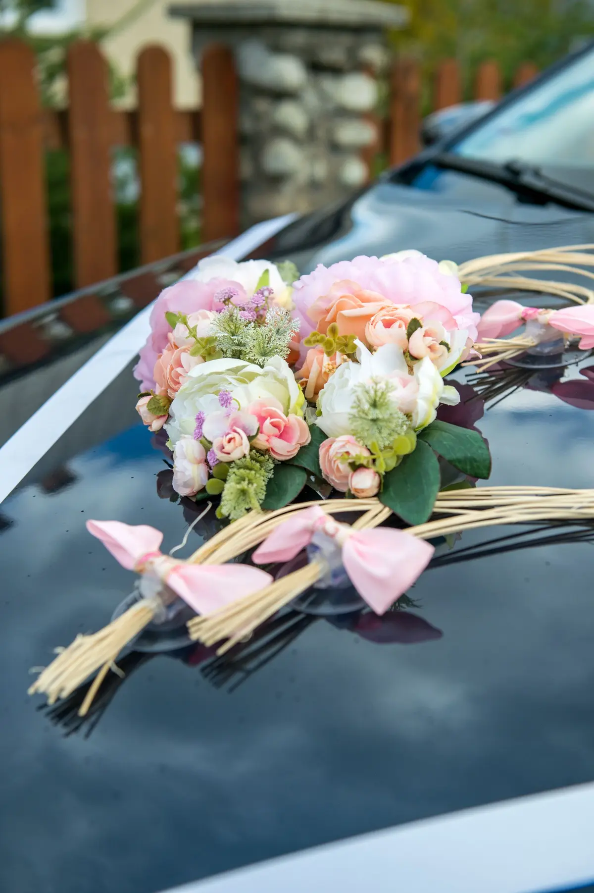 Light-colored flower arrangement and pink ribbons on the hood of a wedding car