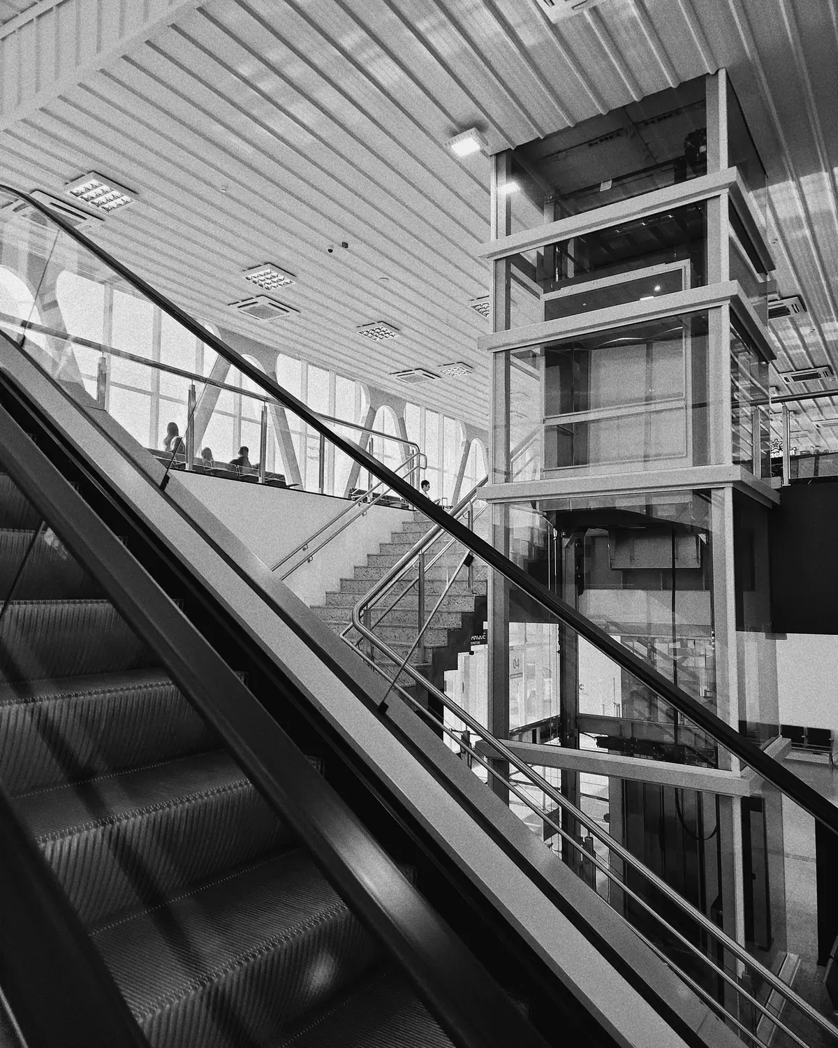Hall of Guarulhos International Airport, with escalators and a glass elevator, in black and white