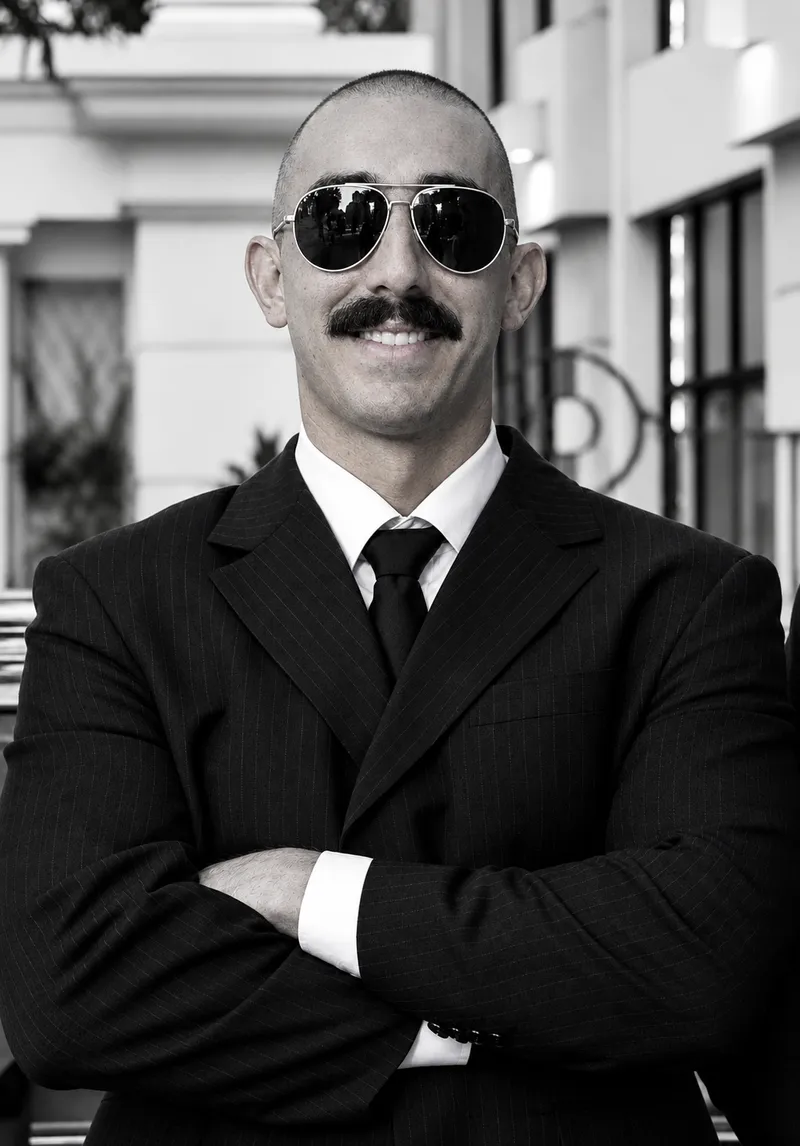 Executive driver in a pinstripe suit, tie and sunglasses, arms crossed, in a black-and-white portrait